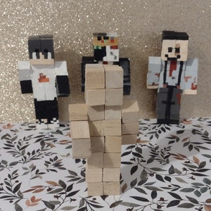 May include: Three Minecraft character figurines, one made of wood blocks, one with a black and white face, and one with a red tie and a bloody face.