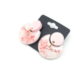 May include: A pair of pink and white earrings with a cherry blossom design. The earrings are made of polymer clay and have a gold hook.