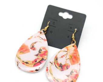 May include: A pair of teardrop-shaped earrings with a pink background and a gold, red, and orange floral design featuring koi fish.