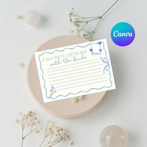 May include: A white card with the text "FAVORITE MEMORY with the bride" in blue script. The card has a blue border, lines for writing, and decorative blue floral and heart accents. The card is on a beige plate.