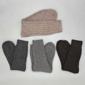 Könnte beinhalten: Eine Sammlung von vier Paar gerippten Socken in neutralen Farbtönen. Ein Paar ist hellbeige, eines ist dunkel anthrazitgrau, eines ist mittelgrau meliert und eines ist dunkelbraun. Jedes Paar weist durchgehend eine vertikale Rippstrickstruktur auf.
