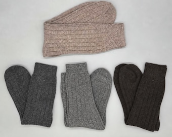 May include: A collection of four pairs of ribbed socks in neutral tones. One pair is a light beige, one is a dark charcoal gray, one is a medium heather gray, and one is a deep brown. Each pair features a vertical ribbed knit texture throughout.