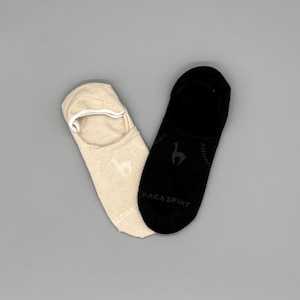 May include: A pair of no-show socks, one beige and one black, with the Alpaca Sport logo. The beige sock has a white elastic band at the opening. The black sock has the Alpaca Sport logo and text.