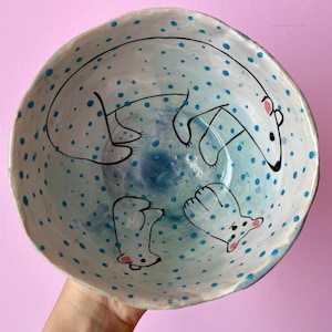 Puede incluir: Un tazón de cerámica blanco con un patrón de lunares azules y blancos. El tazón está decorado con osos polares pintados a mano.