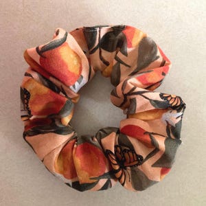 May include: A peach-colored scrunchie with a floral print featuring orange and yellow fruit, green leaves, and brown butterflies.