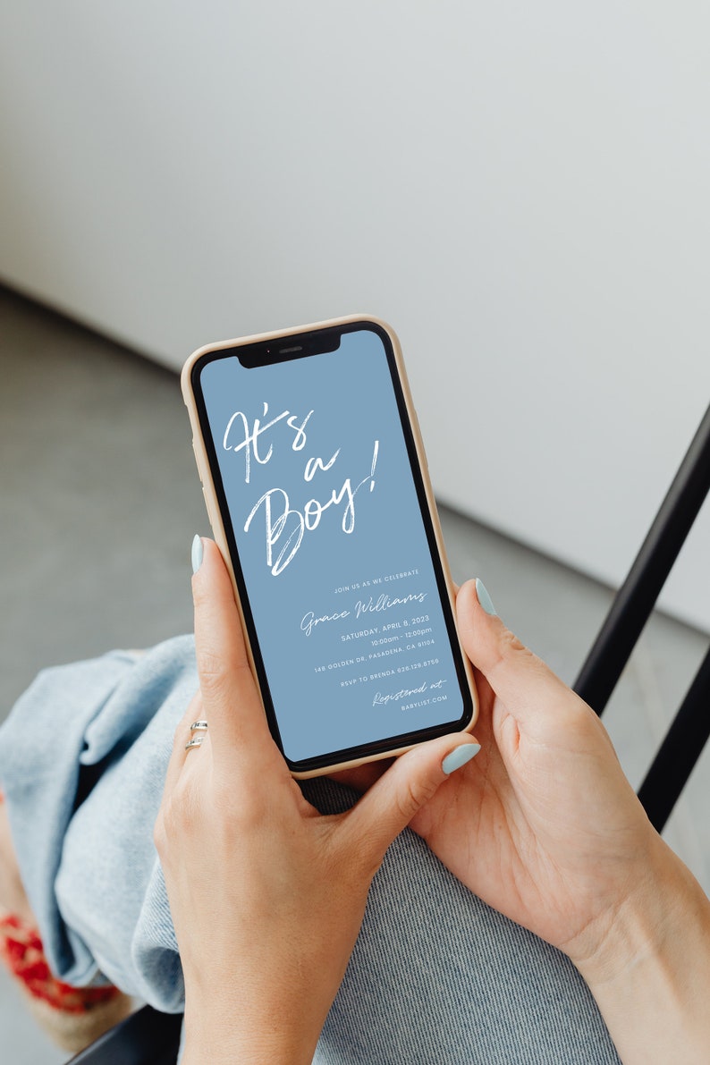 May include: A smartphone displaying a baby shower invitation with a blue background and white text that reads "It's a Boy!" The invitation includes the name "Grace Williams", the date "Saturday, April 8, 2023", the time "10:00am-12:00pm", the location "148 Golden Dr Pasadena, CA 91104", the RSVP information "RSVP to Brenda 628-129-8760", and the website "Registered at Babylist.com".