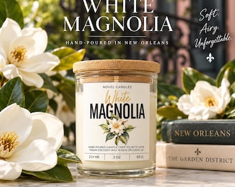 May include: A clear glass candle jar with a bamboo lid, labeled White Magnolia, containing 3 oz of wax. The label features a magnolia flower illustration and text stating it is hand-poured in New Orleans with 100% vegan cocosoy wax.