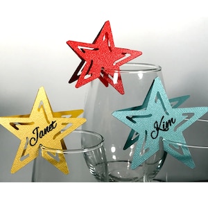 May include: Three star-shaped place cards in red, yellow, and blue. The place cards are made of paper and have names written on them: Janet, Kim, and an unreadable name.
