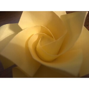 May include: A yellow origami rose made from paper. The rose is folded into a spiral shape, creating a three-dimensional effect.
