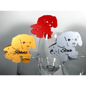 May include: Three dog-shaped place card holders in red, gold, and silver. The place cards are on wine glasses and have the names "Robert" and "Steve" written on them.