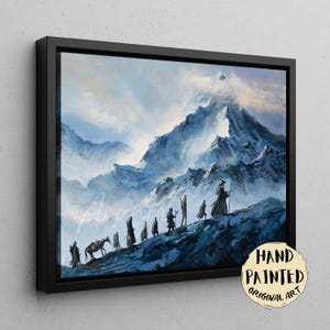 May include: A framed landscape painting depicting a group of small figures travelling along a snowy mountain ridge towards a large, snow-capped peak. The scene features cool blue and white tones with a circular sticker reading HAND PAINTED ORIGINAL ART.