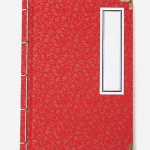 Puede incluir: Diario rojo cubierto de tela con un diseño de esquina de metal dorado y una etiqueta blanca con borde negro.