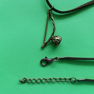 Puede incluir: Un collar de cord&oacute;n de cuero marr&oacute;n con un colgante de metal con forma de berimbau, un instrumento musical brasile&ntilde;o. El collar tambi&eacute;n incluye un cierre de metal y una extensi&oacute;n de cadena.
