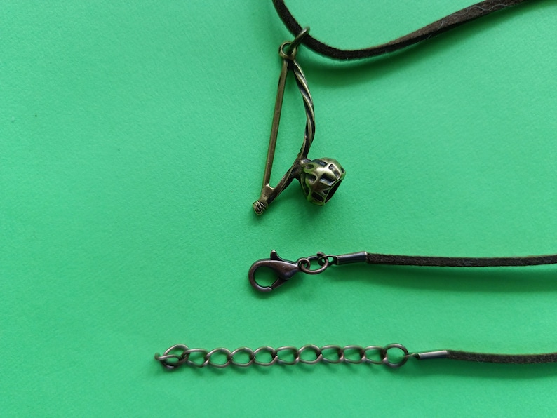 Puede incluir: Un collar de cord&oacute;n de cuero marr&oacute;n con un colgante de metal con forma de berimbau, un instrumento musical brasile&ntilde;o. El collar tambi&eacute;n incluye un cierre de metal y una extensi&oacute;n de cadena.