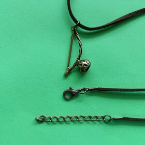 Puede incluir: Un collar de cord&oacute;n de cuero marr&oacute;n con un colgante de metal con forma de berimbau, un instrumento musical brasile&ntilde;o. El collar tiene un cierre de metal y una cadena de extensi&oacute;n.