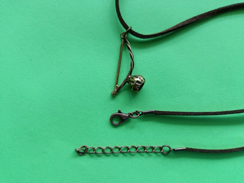 Puede incluir: Un collar de cord&oacute;n de cuero marr&oacute;n con un colgante de metal con forma de berimbau, un instrumento musical brasile&ntilde;o. El collar tiene un cierre de metal y una cadena de extensi&oacute;n.