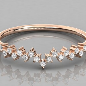 May include: Rose gold ring with a curved design. The ring features a series of small, sparkling white gemstones set along the curve. The gemstones are evenly spaced and add a touch of elegance to the ring's design.