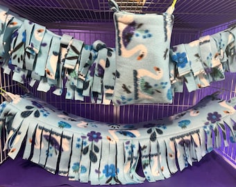May include: A blue and white fleece hammock with fringe, a blue and white fleece hanging pouch, and a blue and white fleece hanging toy for small animals. The hammock and pouch have a floral pattern with white swans.