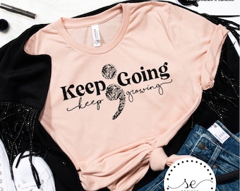 May include: A pink t-shirt with black text that reads "Keep Going keep growing" with a semicolon design in the middle of the text. The semicolon is made up of black floral designs.