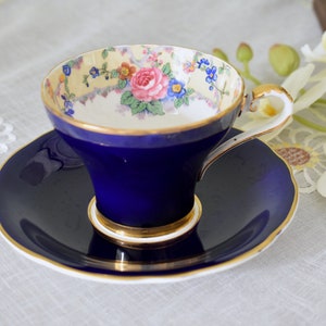 May include: A blue and gold teacup and saucer set with a floral pattern. The teacup has a white interior with a floral design and a gold rim. The saucer is a solid blue with a gold rim.