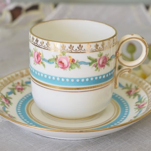 Peut inclure: Une tasse à thé et une soucoupe en porcelaine blanche avec un motif floral bleu et or. La tasse a une poignée délicate et la soucoupe a un bord festonné.