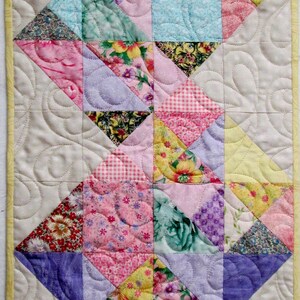 May include: A patchwork quilt with a variety of floral and geometric patterns in pink, yellow, blue, green, and purple. The quilt is made of squares and triangles and is quilted with a swirl pattern.