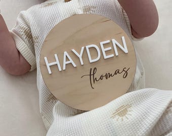 May include: A round wooden sign with the name "HAYDEN Thomas" written in white and brown lettering.