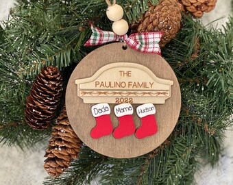 May include: A wooden Christmas ornament with the text "The Paulino Family 2022" and three red stockings with the names "Dada", "Mama", and "Hudson" written on them.