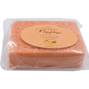 May include: A bar of orange-colored soap wrapped in plastic. The label reads "Pee's 100% Handmade Mango Pineapple Body Soap Vegan & Cruelty-Free Net Weight 4.5 oz".