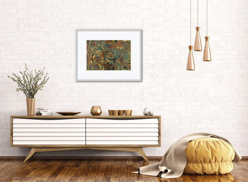 May include: A framed print of a marbled design with swirls of blue, green, yellow, and brown. The print is hanging on a white brick wall above a white dresser with a wooden top.