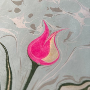 May include: A pink and gold tulip flower design on a light blue marbled background.