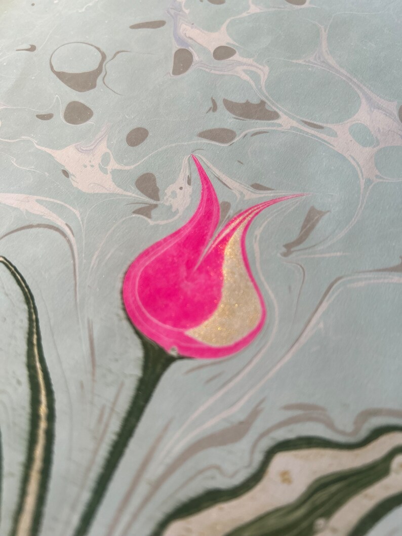 May include: A pink and gold tulip flower design on a light blue marbled background.