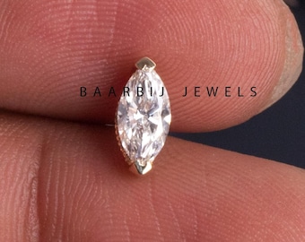 May include: A marquise-shaped clear gemstone set in a gold setting. The gemstone is held in a person's hand.