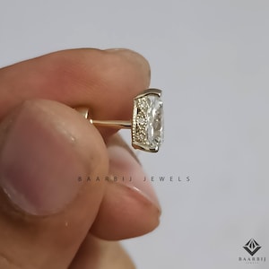 K&ouml;nnte beinhalten: Nahaufnahme eines goldenen Ohrrings mit einem rechteckigen, klaren Edelstein. Der Ohrring hat einen kleinen, dekorativen Rand um den Edelstein. Der Text "BAARBIJ JEWELS" ist darunter gedruckt.