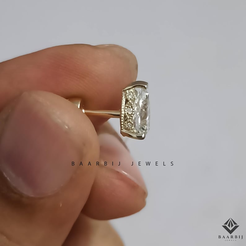 K&ouml;nnte beinhalten: Nahaufnahme eines goldenen Ohrrings mit einem rechteckigen, klaren Edelstein. Der Ohrring hat einen kleinen, dekorativen Rand um den Edelstein. Der Text "BAARBIJ JEWELS" ist darunter gedruckt.