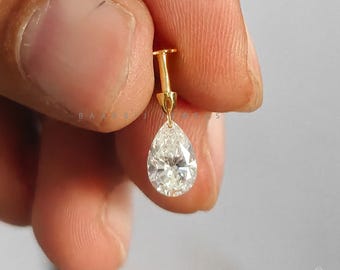 May include: A gold stud earring featuring a pear-shaped, faceted clear gemstone suspended from a vertical gold post. The jewelry piece displays a brilliant cut stone that reflects light, attached to a small, polished gold metal base.