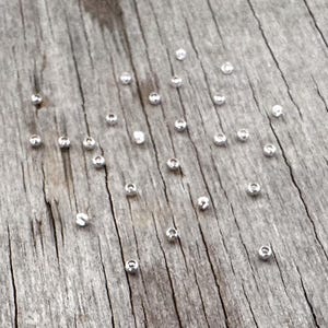 May include: A collection of small, clear, round beads scattered on a weathered, gray wooden surface. The beads are evenly spaced and appear to be made of glass or a similar transparent material. The wood grain is visible, adding texture to the image.