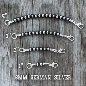 May include: Four silver-toned beaded chain extenders, 1 to 4 inches long, with lobster claw clasps and jump rings. The beads are 6mm German silver. The extenders are displayed on a weathered wood surface.