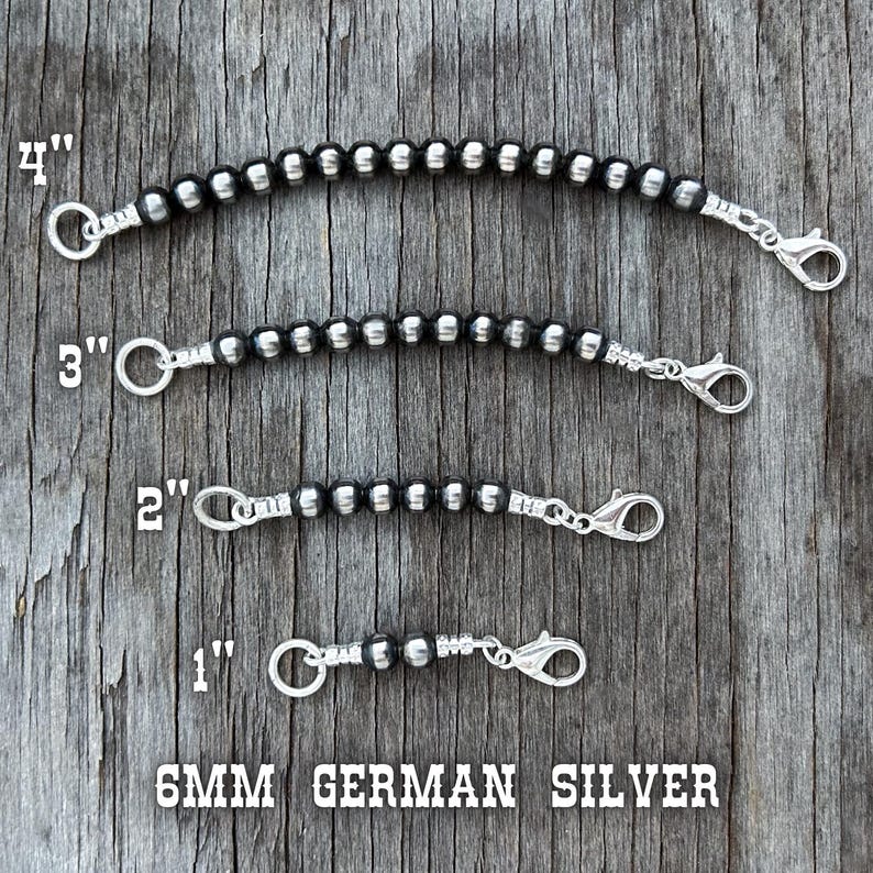 May include: Four silver-toned beaded chain extenders, 1 to 4 inches long, with lobster claw clasps and jump rings. The beads are 6mm German silver. The extenders are displayed on a weathered wood surface.
