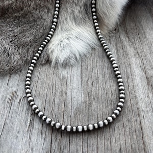 May include: A necklace composed of a single strand of uniform, polished silver-toned spherical beads. The beads are arranged in a continuous circular pattern, reflecting light on their smooth, metallic surfaces, creating a consistent and simple design.