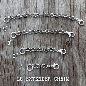 May include: Four silver-colored extender chains of varying lengths, 1 to 4 inches, with lobster claw clasps and circular ring connectors. The chains are displayed on a wooden surface. The text "LG EXTENDER CHAIN" is at the bottom.