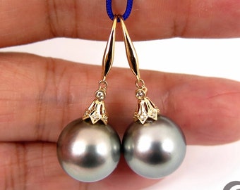 May include: A pair of gold dangle earrings with black pearls and small diamonds. The earrings are hanging from a blue cord.