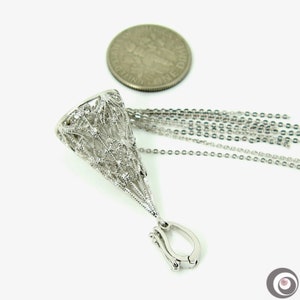 May include: A silver-colored pendant necklace with a detailed, openwork cone design. The pendant is attached to multiple delicate chains and a clasp. A dime is placed near the pendant for size comparison. The necklace is on a white background.
