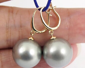 May include: A pair of gold hoop earrings with large, round, gray pearls hanging from them.