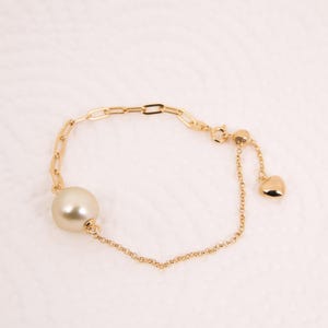 May include: A gold chain bracelet featuring a large pearl and a small heart charm.