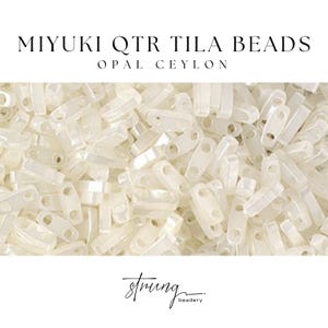 Op de afbeelding: Close-up van een stapel Miyuki QTR Tila kralen in Opal Ceylon. De kralen zijn rechthoekig met twee gaten en een licht doorschijnende, gebroken witte kleur. De tekst "MIYUKI QTR TILA BEADS" en "OPAL CEYLON" staat bovenaan. Het logo "strung beadery" staat onderaan.