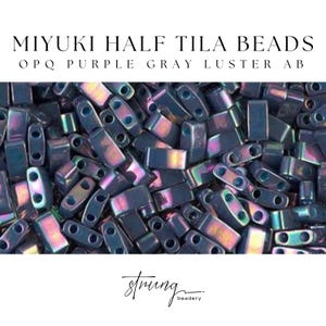 Könnte beinhalten: Nahaufnahme von Miyuki Half Tila Perlen in OPQ Purple Gray Luster AB. Die rechteckigen Perlen mit zwei Löchern haben ein metallisches Finish mit violetten, grauen und irisierenden Farbtönen. Das Bild enthält den Text "MIYUKI HALF TILA BEADS" und "strung beadery".