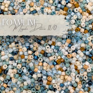 May include: A collection of small, cylindrical beads in various shades of blue, cream, and brown. The beads are scattered, creating a textured surface. The text "FOAMLINE Miyuki Delica 11/0" is visible in the image.