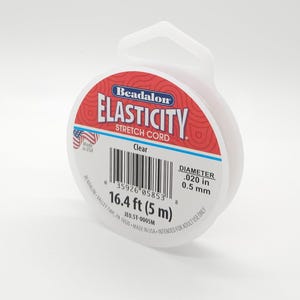 May include: Clear Beadalon Elasticity stretch cord. The spool has a diameter of 0.5 mm and contains 5 m of cord. The label is red and white with the brand name and product details.