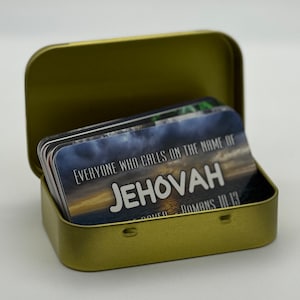 May include: A gold metal tin with a hinged lid containing a stack of cards with a sunset background and the text "Everyone who calls on the name of JEHOVAH is saved - Romans 10:13"